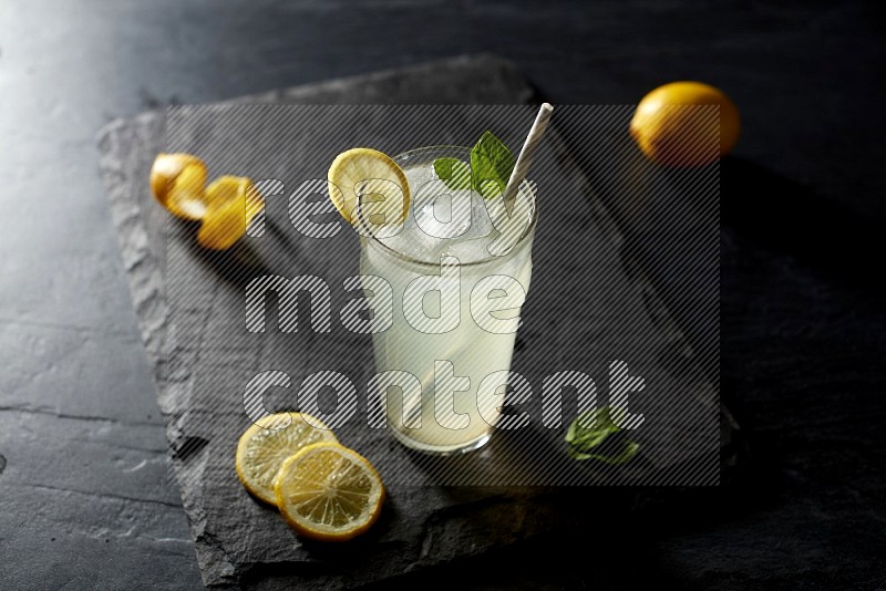 A glass of lemon juice with a straw on black background