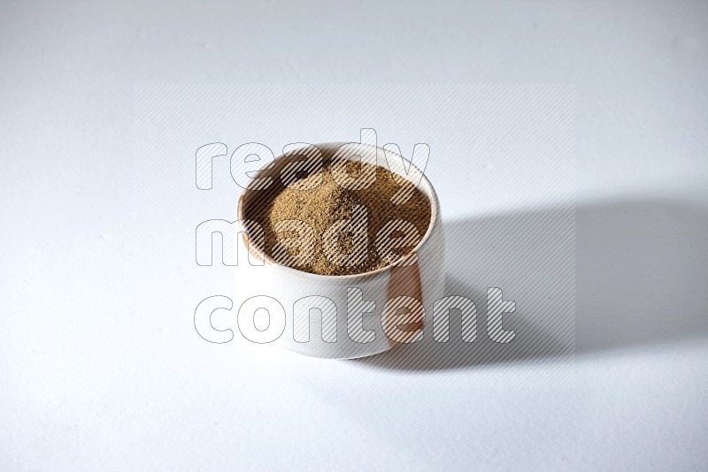 A beige bowl full of cumin powder on a white flooring