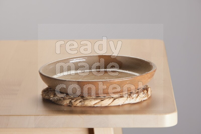 multi-colored pottery Plate placed on a small light colored straw placemat on the edge of wooden table