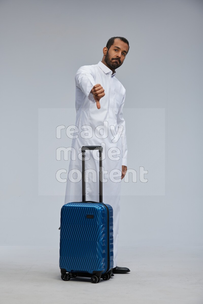 Saudi man wearing thob standing holding Travel bag on Gray background