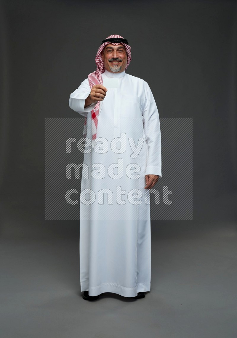 Saudi man with shomag Standing holding ATM card on gray background
