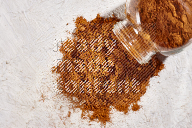 A glass jar full of ground paprika powder flipped with some spilling powder on white background