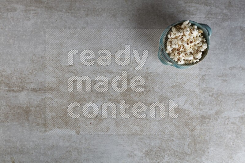 popcorn in a multi-colored handheld ceramic bowl on a grey textured countertop