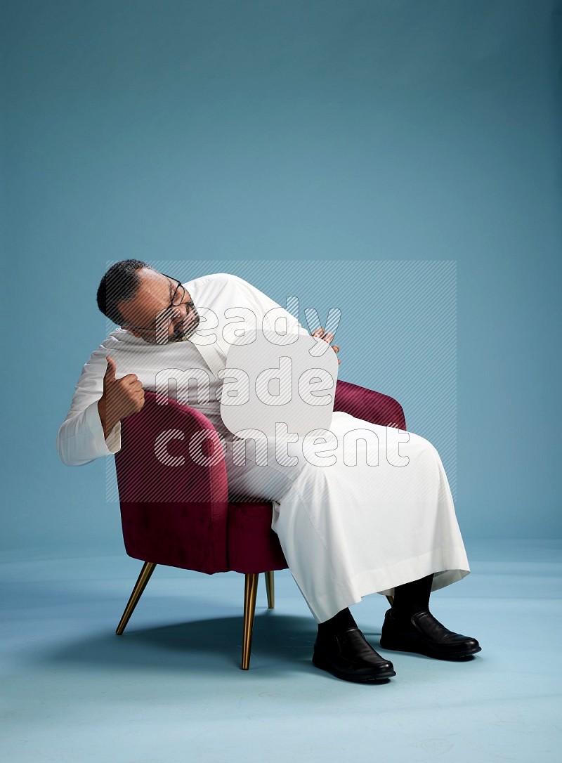 Saudi Man without shimag sitting on chair holding social media sign on blue background