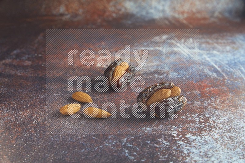 two almond stuffed madjoul dates on a rustic reddish background