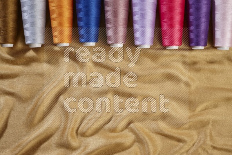 Multicolored sewing thread spools on yellow fabric background