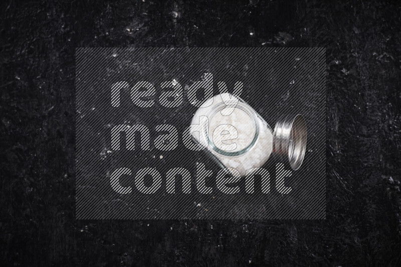 وعاء زجاجي ممتلئ بملح البحر الخشن على خلفية سوداء