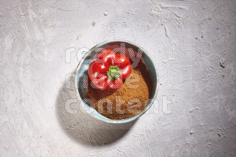 A colored pottery plate full of ground paprika powder and red bell pepper on white background