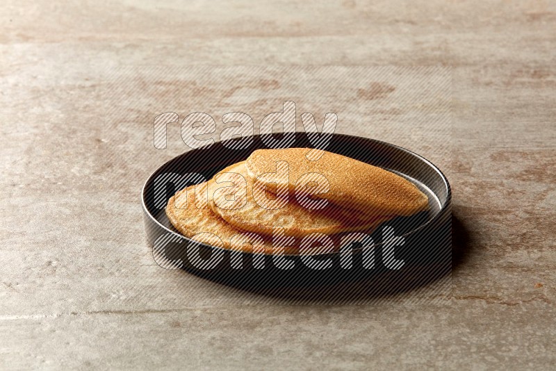 Three stacked plain pancakes in a black plate on beige background