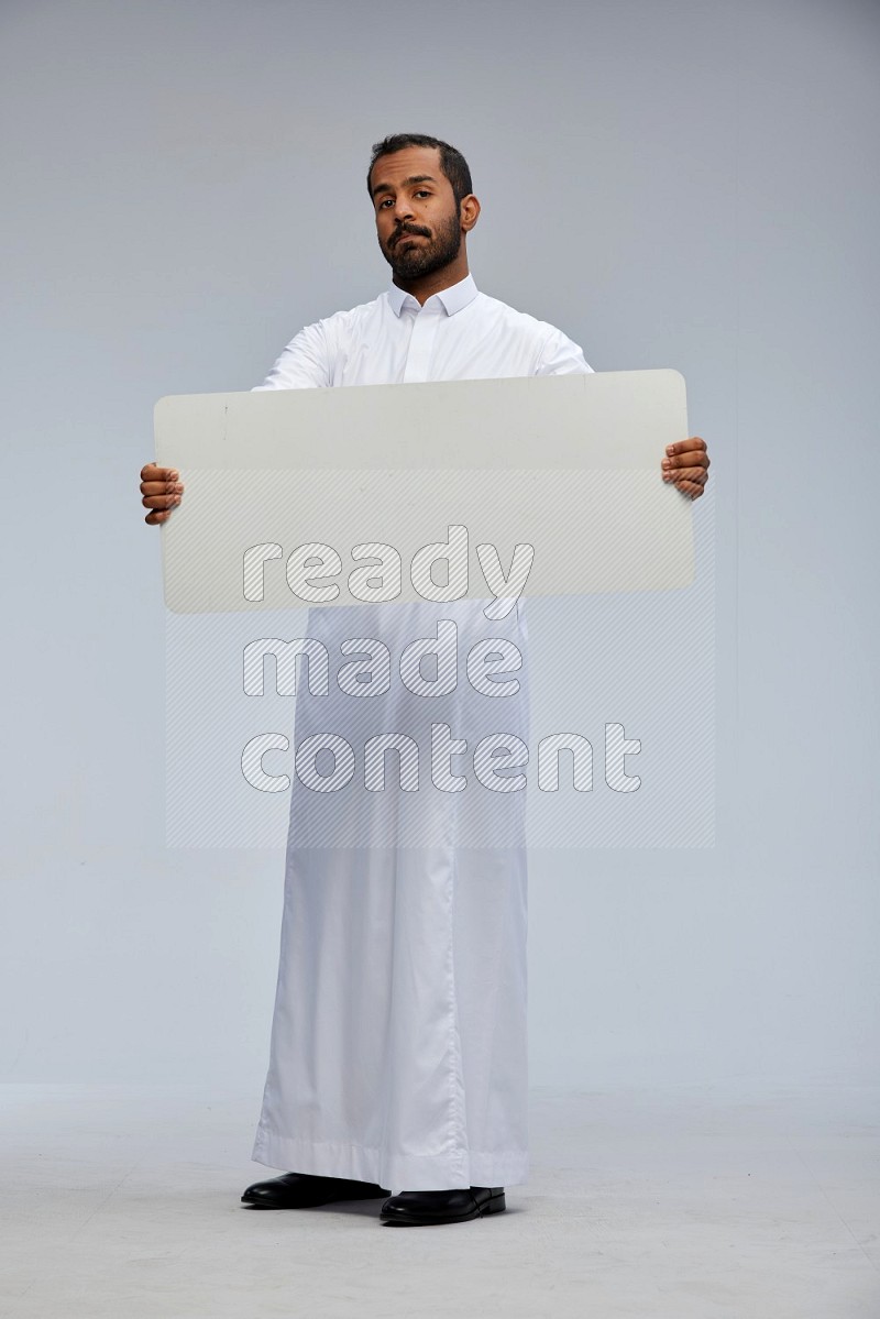 Saudi man wearing Thob standing holding board on Gray background