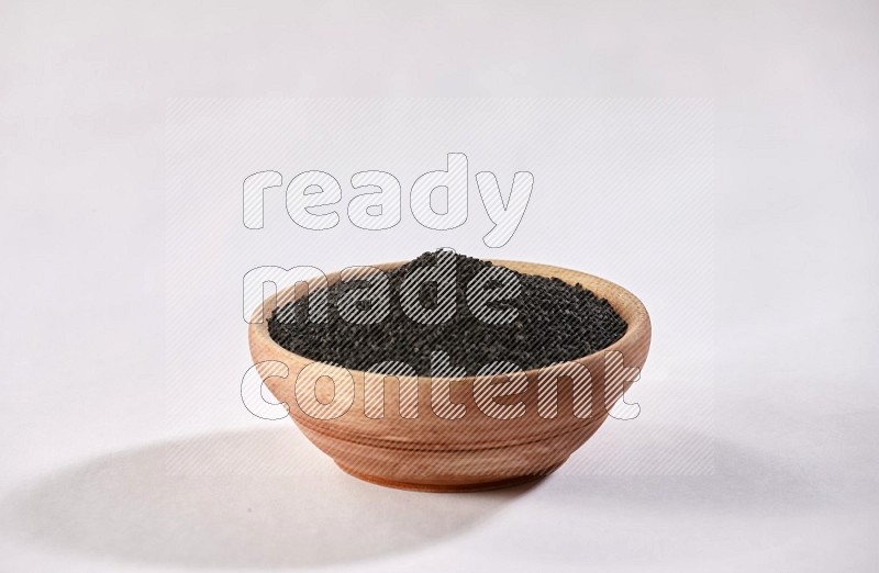 وعاء خشبي ممتلئ ببذور حبة البركة علي خلفية بيضاء