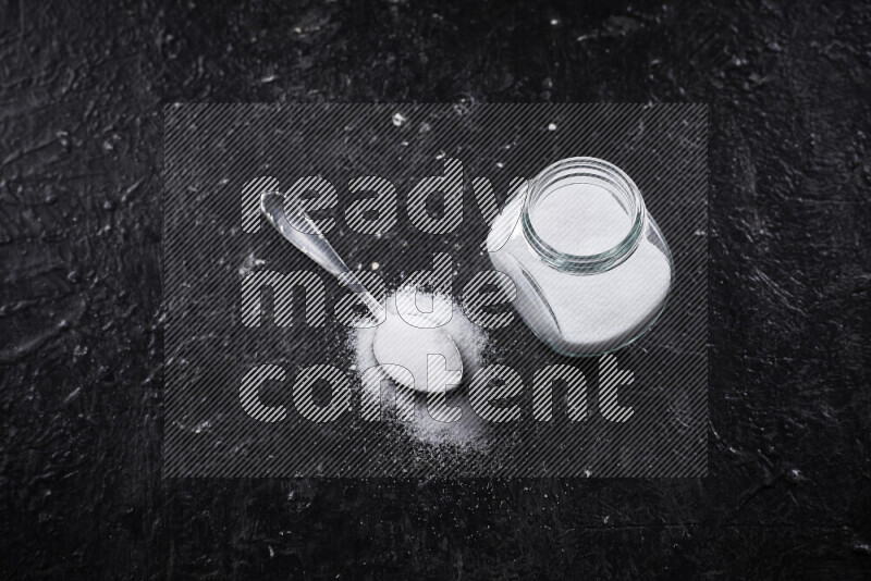 A glass jar full of fine table salt on black background