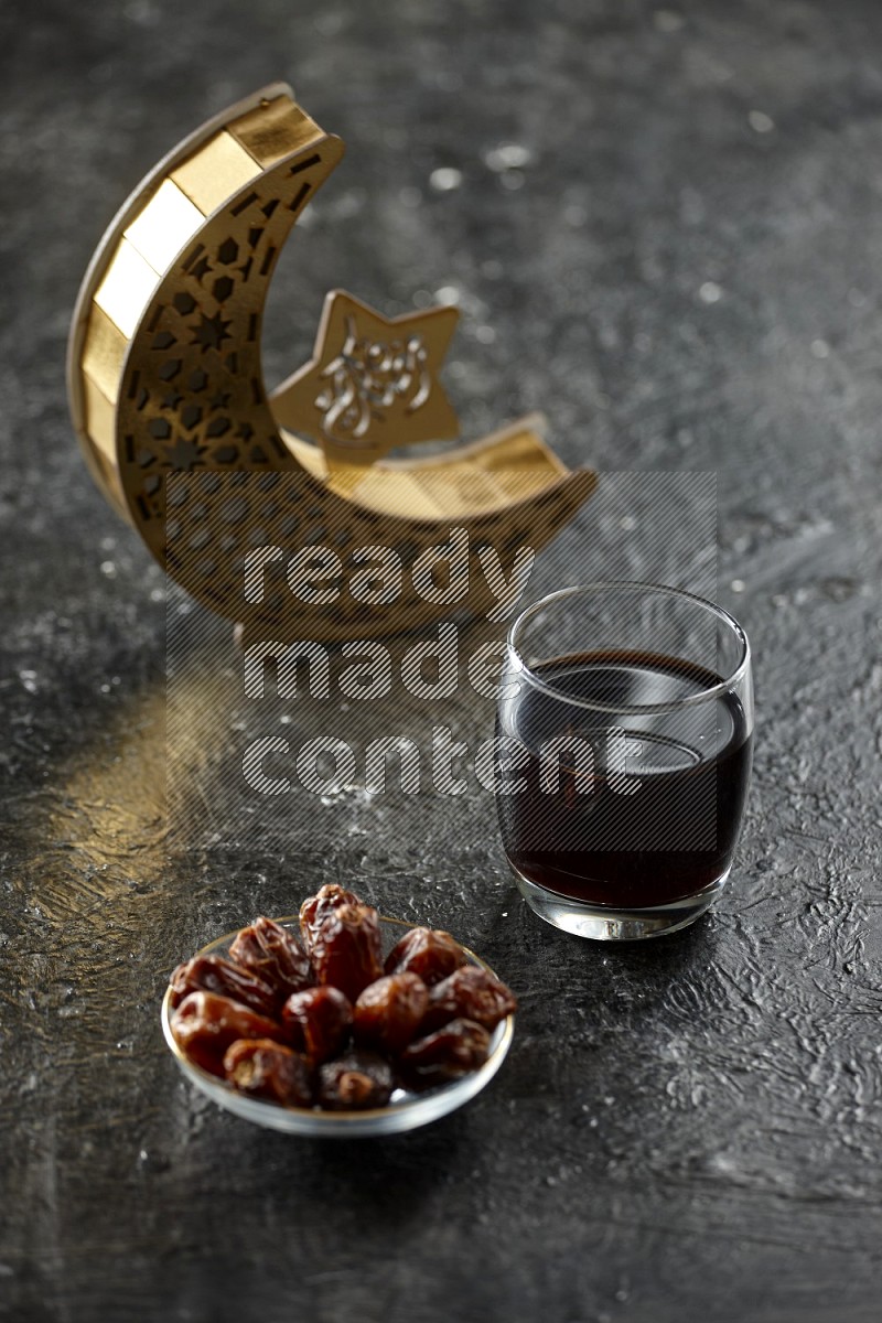 A wooden golden crescent lantern with different drinks, dates, nuts, prayer beads and quran on textured black background