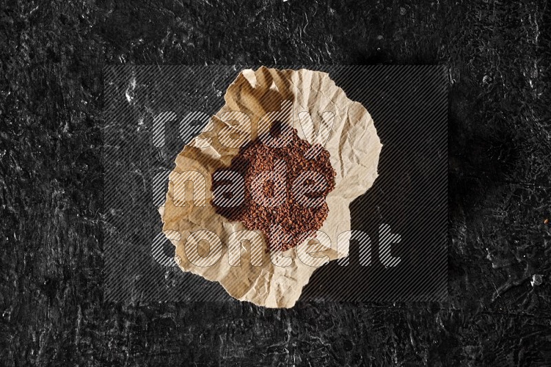 A crumpled piece of paper full of garden cress seeds on a textured black flooring