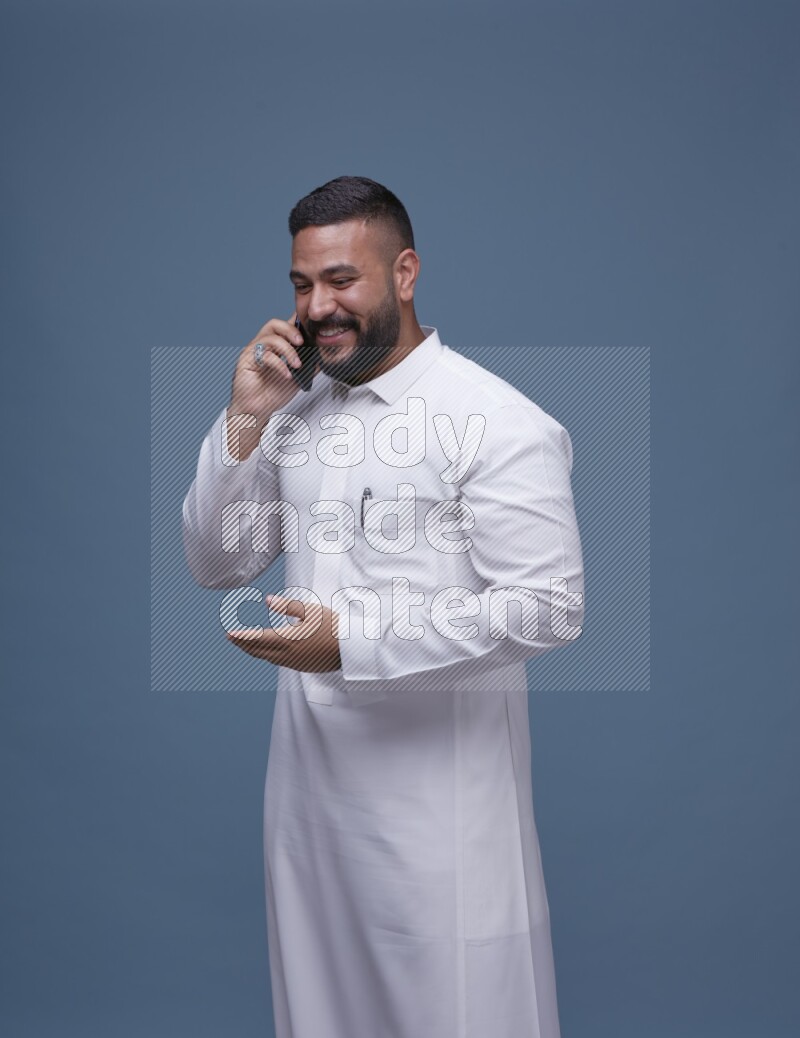 A Saudi man calling on blue background wearing Saudi Thob