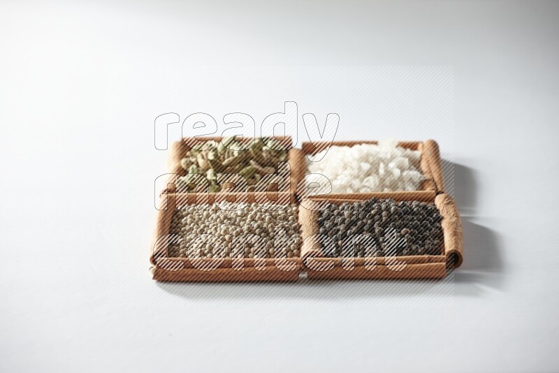 4 مربعات من أعواد القرفة ممتلئة بالهيل والملح والفلفل الأبيض والفلفل الأسود على أرضية بيضاء