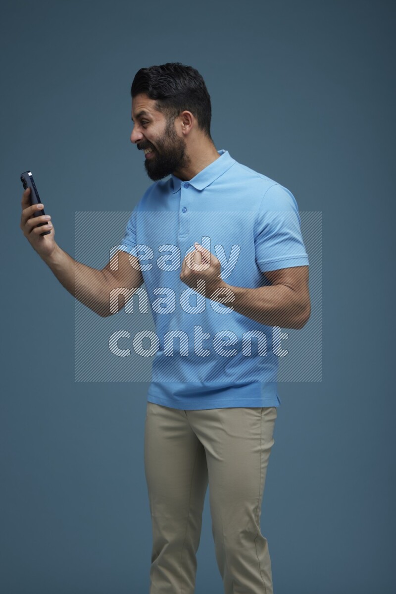 Man posing with a phone in a blue background wearing a Blue shirt