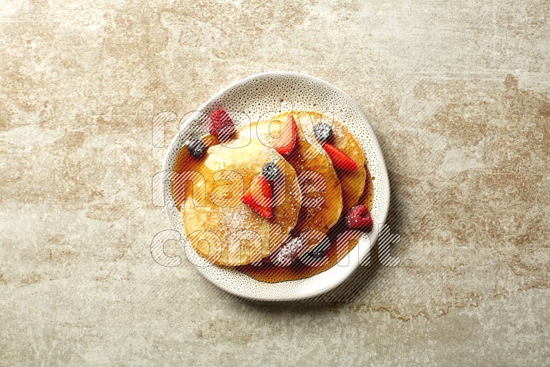 Three stacked mixed berries pancakes in an irregular plate on beige background
