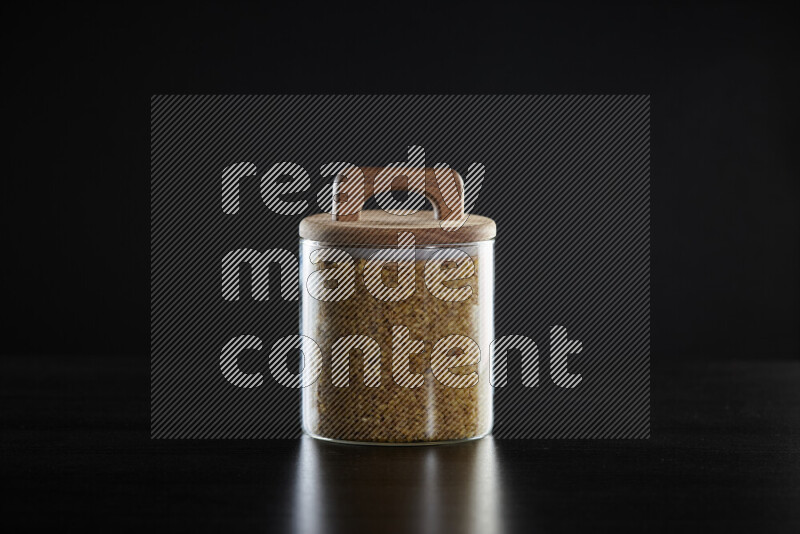 Coarse bulgur in a glass jar on black background