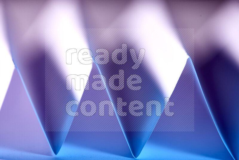 A close-up abstract image showing sharp geometric paper folds in blue and pink gradients