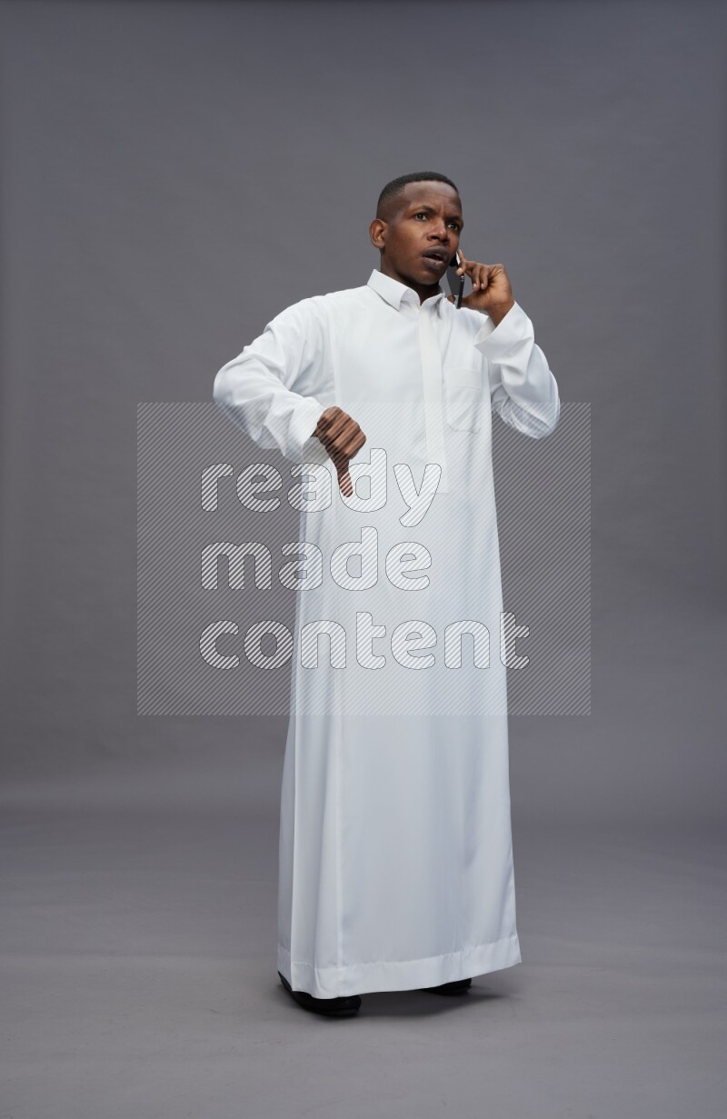 Saudi man wearing thob standing talking on phone on gray background