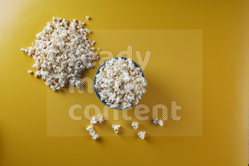 A blue pottery bowl full of popcorn with popcorn beside it on a yellow background in different angles