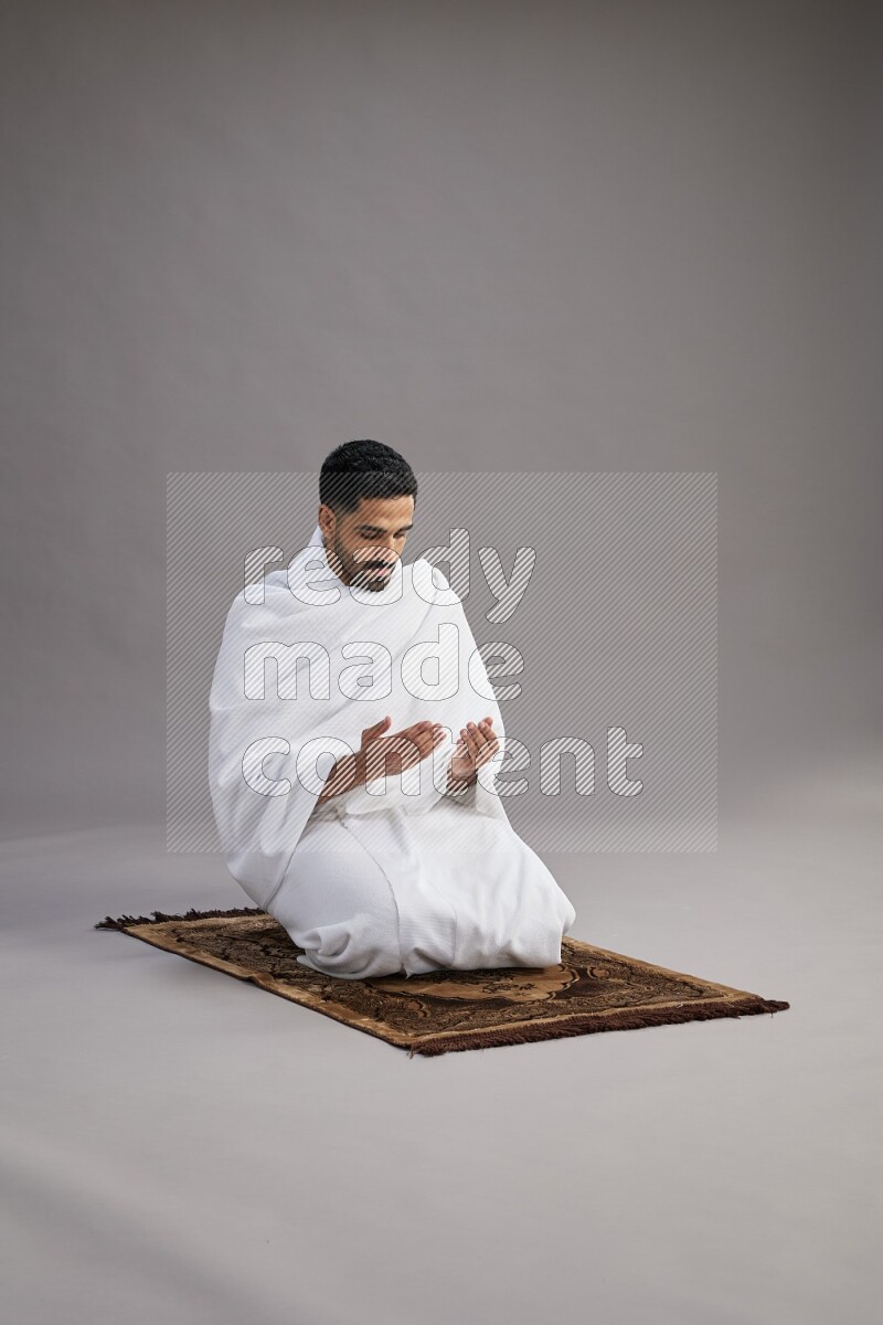 A man wearing Ehram performing dua'a on gray background