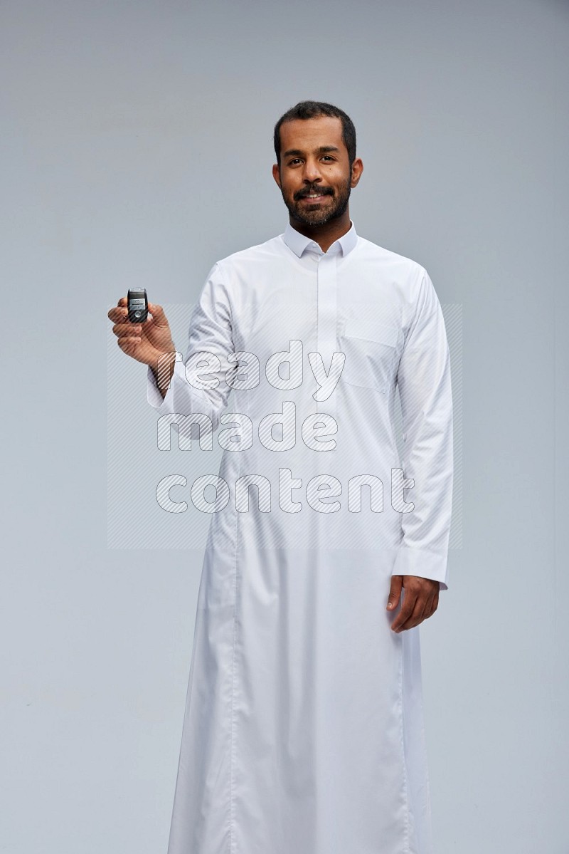 Saudi man wearing thob and shomag standing holding car key on gray background
