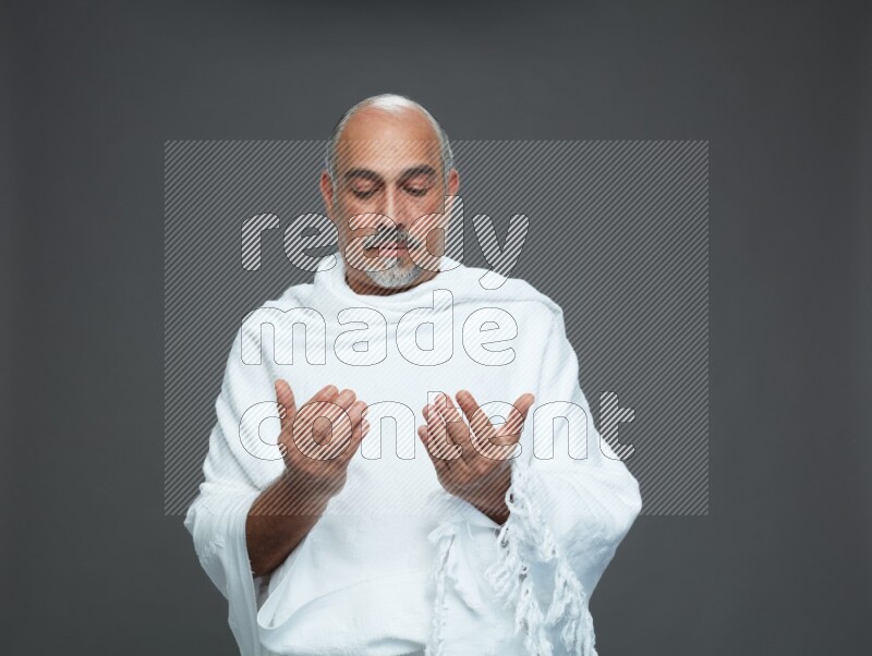 A man wearing Ehram Standing dua'a on gray background