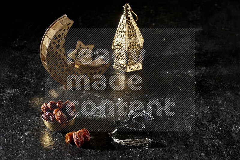 Dates in a metal bowl with prayer beads beside golden lanterns in a dark setup