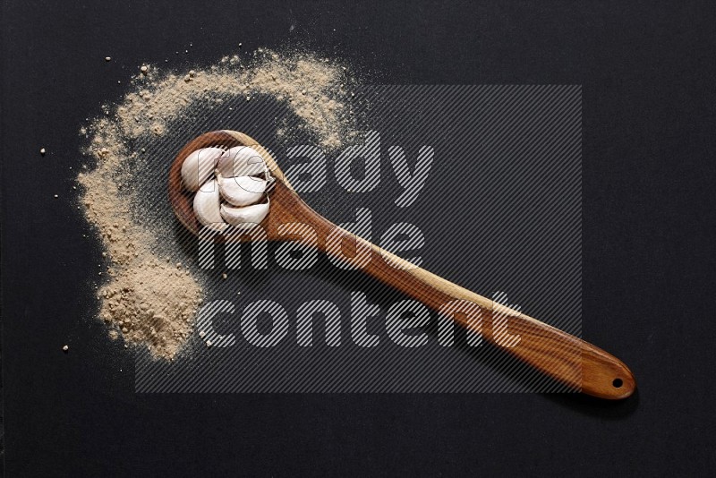 A wooden ladle full of garlic cloves with sprinkled powder on a black flooring in different angles