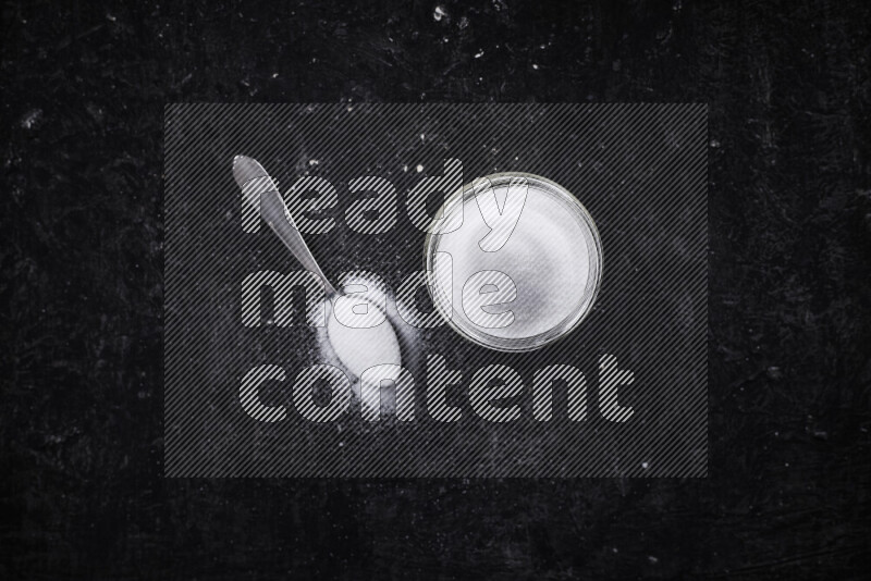 A glass jar full of fine table salt on black background