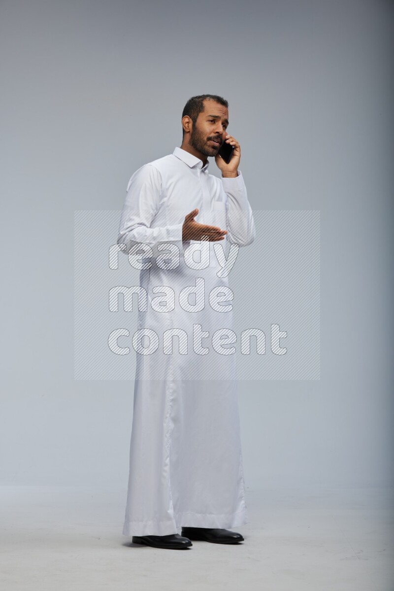 Saudi man wearing Thob standing talking on phone on Gray background