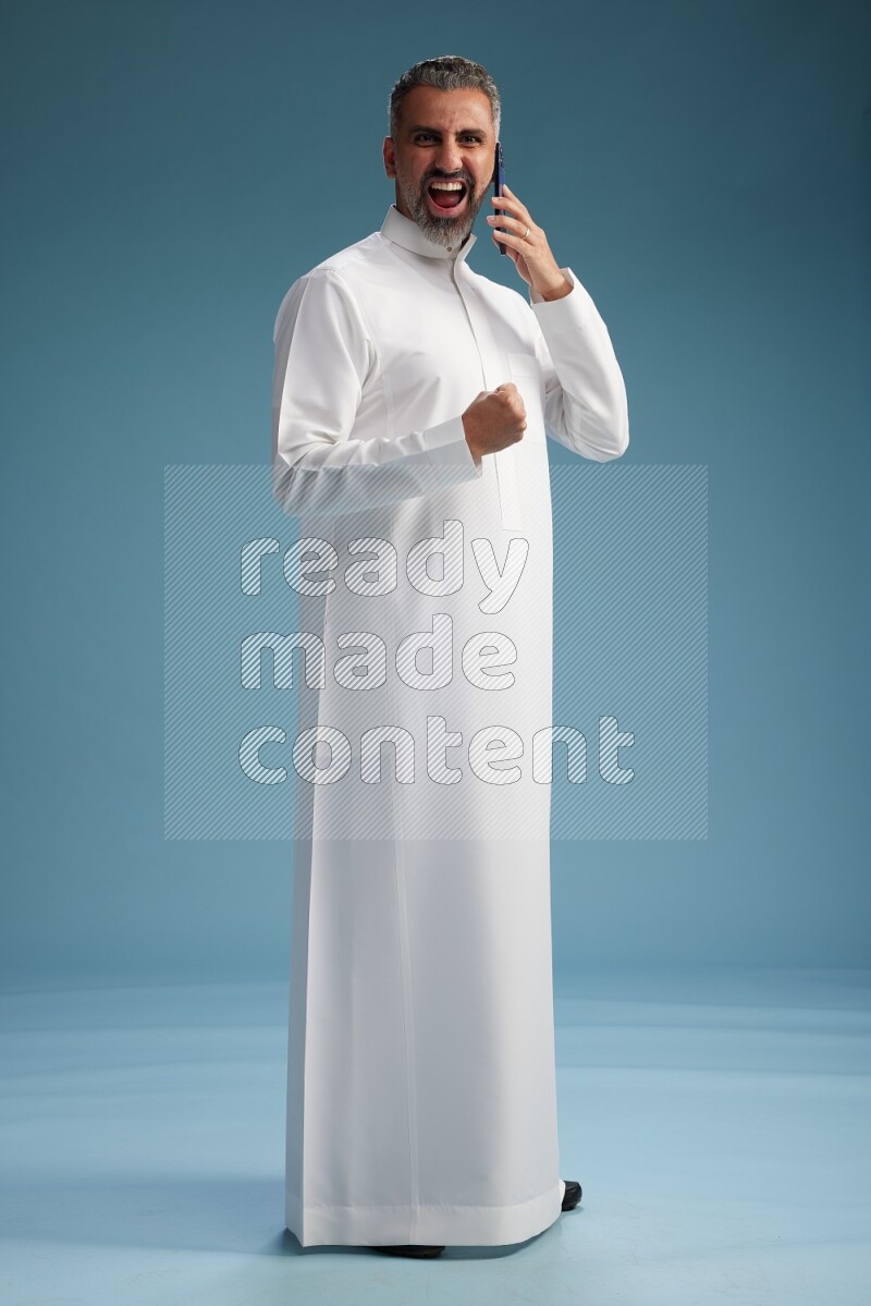 Saudi man wearing thob talking on the phone on blue background