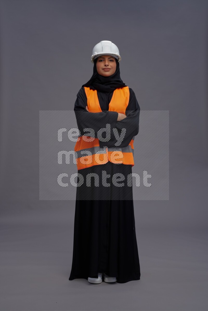 Saudi woman wearing Abaya with engineer vest standing with crossed arms on gray background