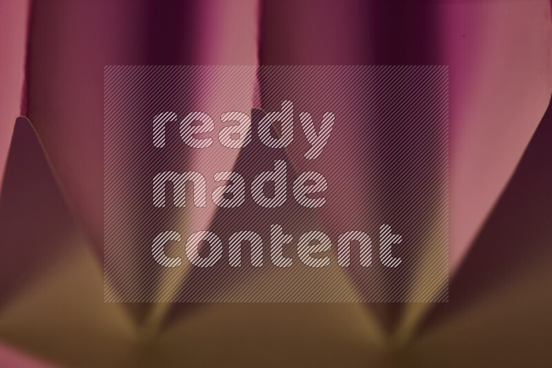 A close-up abstract image showing sharp geometric paper folds in pink gradients and warm tones