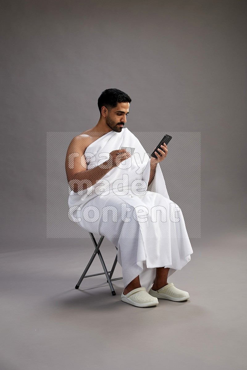 A man wearing Ehram sitting on chair holding ATM card on gray background