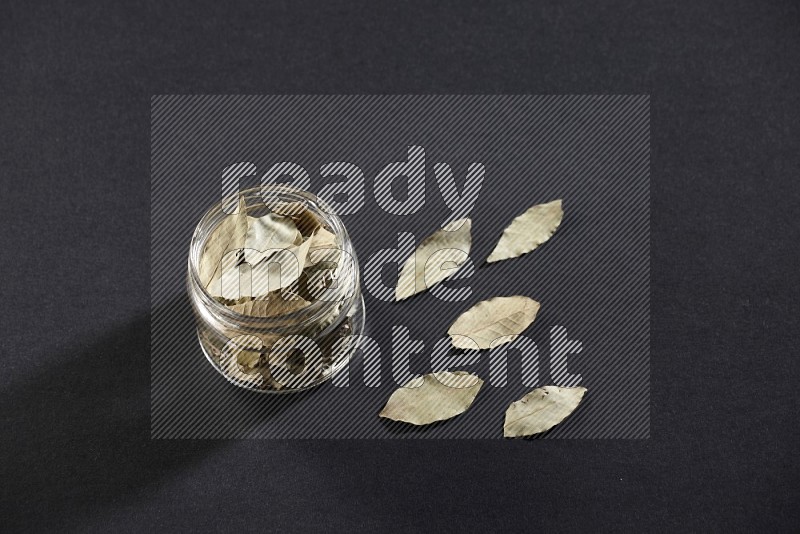 A glass jar filled with dried bay leaves on black flooring