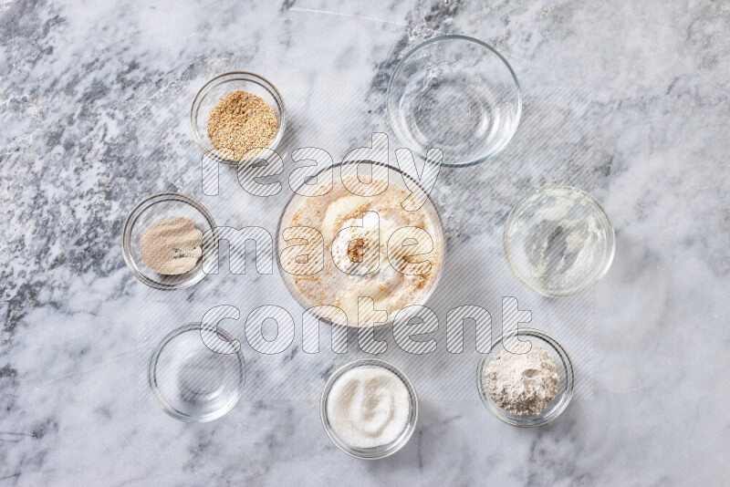 كحك خطوة بخطوة بمكوناته سمن، سكر، دقيق، سمسم، خميرة، ماء ونكهة الكحك على خلفية رخام رمادي