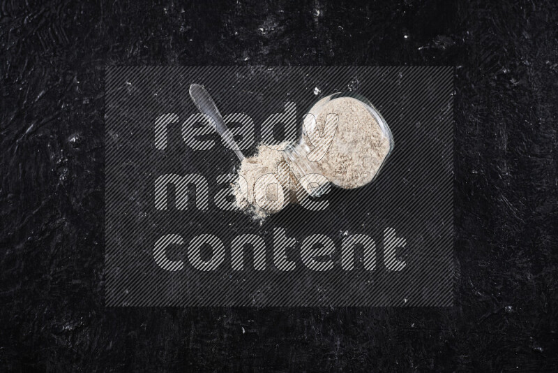 A glass jar full of onion powder flipped with some spilling powder on black background