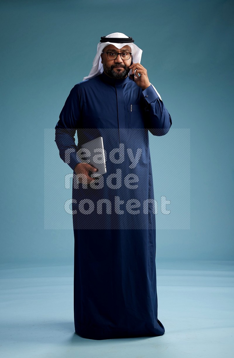 Saudi Man with shimag Standing talking on phone on blue background