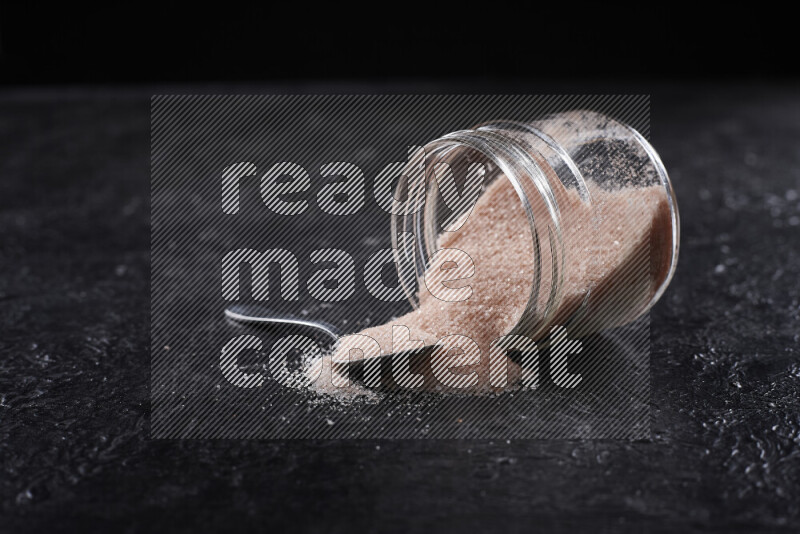 A glass jar full of fine himalayan salt on black background