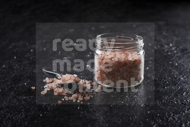 A glass jar full of coarse himalayan salt crystals on black background