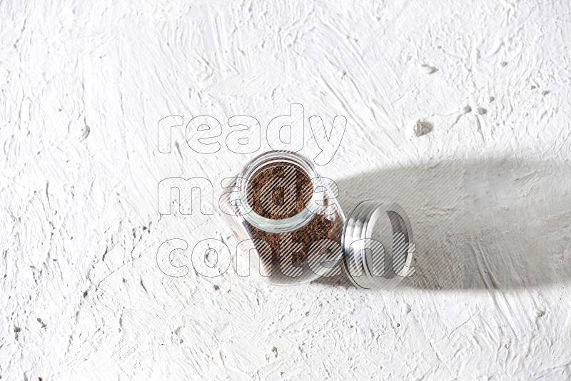 وعاء زجاجي للبهارات ممتلئ ببودرة القرنفل على أرضية بيضاء