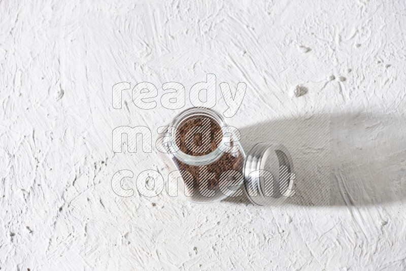 A glass spice jar full of cloves powder on textured white flooring