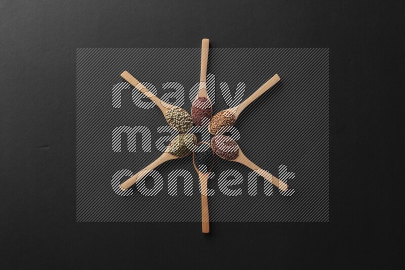 wooden spoons filled with white peppers, mustard seeds, black seeds, garden cress, cumin and flax on black flooring and shaped like a clock