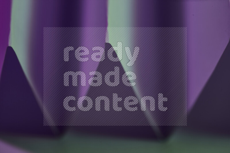 A close-up abstract image showing sharp geometric paper folds in green and purple gradients