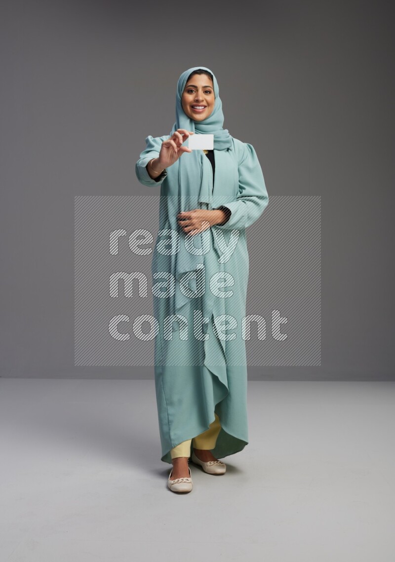 Saudi Woman wearing Abaya standing holding ATM card on Gray background