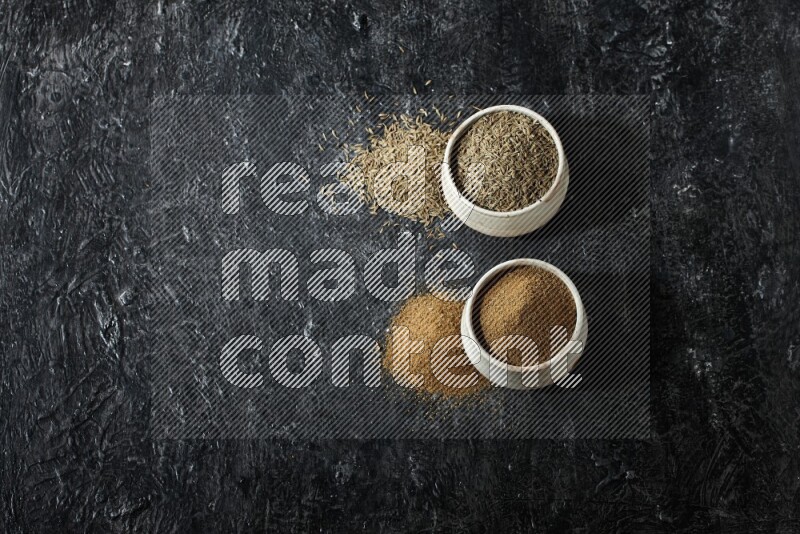 وعاءين بيج، أحدهما ممتلئ ببودرة الكمون والآخر ممتلئ بحبوب الكمون، على خلفية سوداء