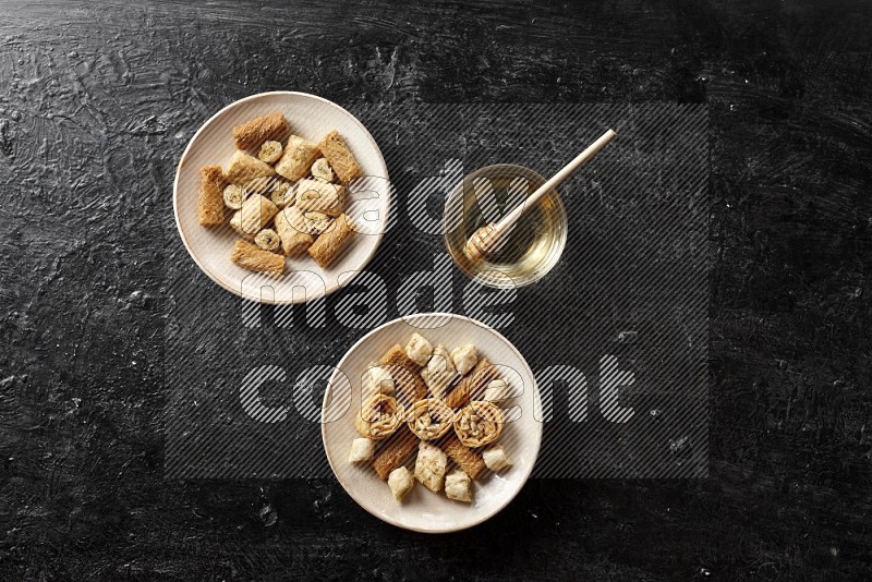 حلويات شرقية في أطباق فخارية مع العسل علي خلفية سوداء خشبية